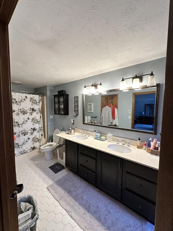 full bath with double vanity, a sink, a textured ceiling, and toilet