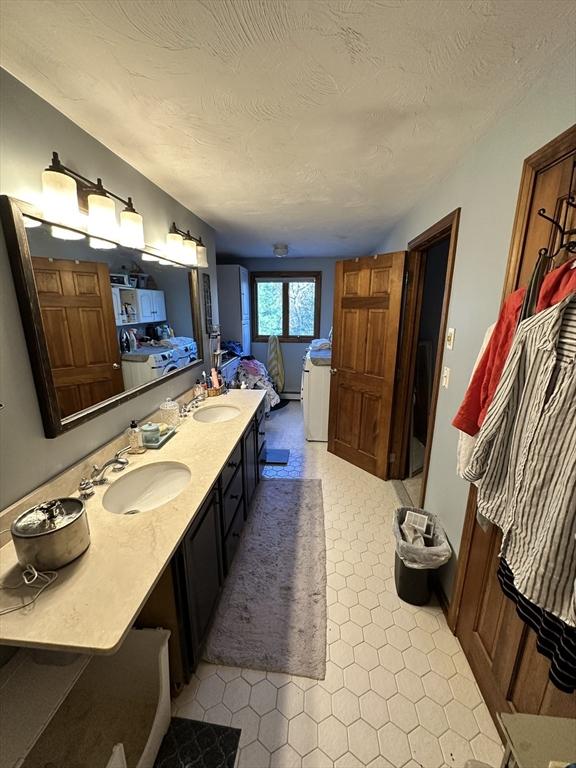 ensuite bathroom with double vanity, a sink, connected bathroom, and a textured ceiling