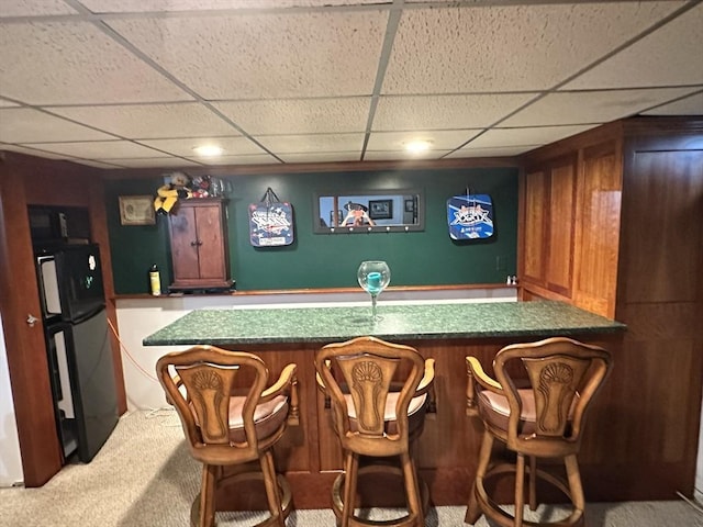 bar with a bar, fridge, carpet flooring, and a paneled ceiling