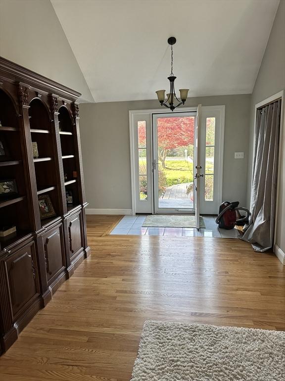 foyer with light wood-type flooring, baseboards, a chandelier, and vaulted ceiling