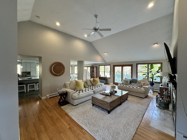 living area featuring baseboard heating, high vaulted ceiling, a ceiling fan, baseboards, and wood finished floors