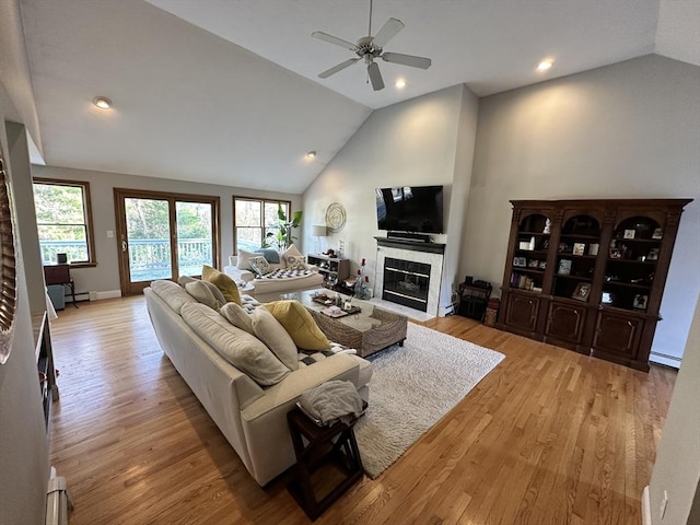 living area with light wood-style flooring, ceiling fan, vaulted ceiling, and a fireplace