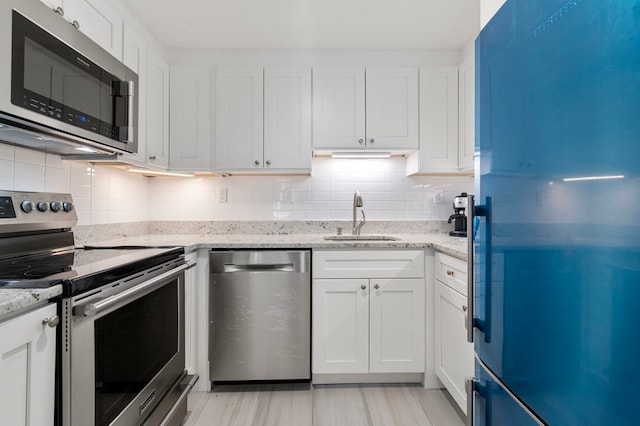 kitchen featuring sink, light stone counters, white cabinets, stainless steel appliances, and tasteful backsplash