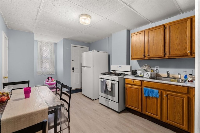 kitchen with white appliances, brown cabinets, light countertops, light wood-type flooring, and a sink