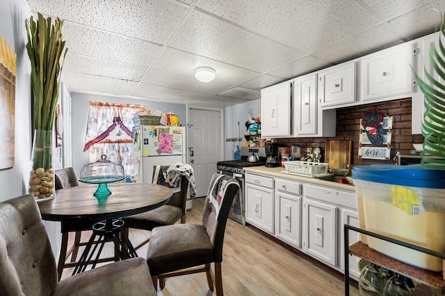 kitchen with stainless steel gas stove, a drop ceiling, light countertops, light wood-style floors, and white cabinetry