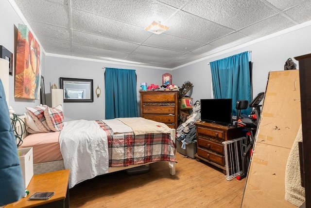 bedroom with ornamental molding, light wood-type flooring, and a paneled ceiling