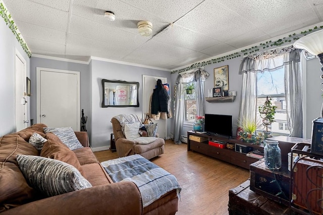 living area with ornamental molding, a paneled ceiling, baseboards, and wood finished floors