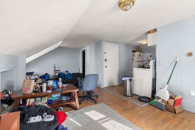 interior space with washer / dryer, a textured ceiling, vaulted ceiling, and wood finished floors