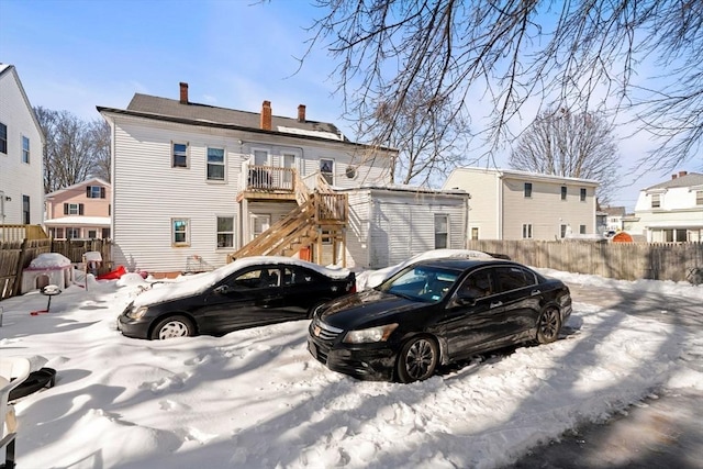 snow covered property with fence, a chimney, and stairs