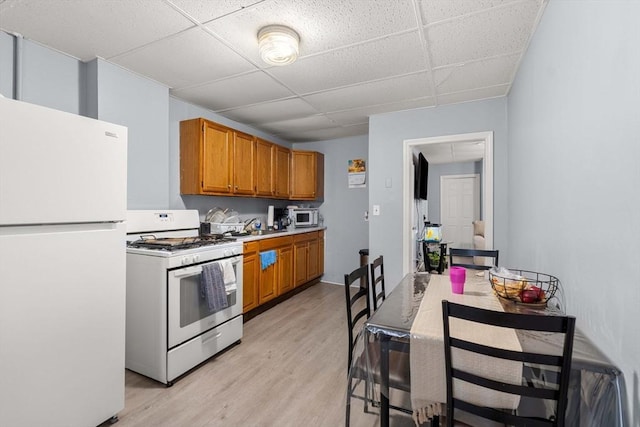 kitchen with brown cabinetry, white appliances, light countertops, and light wood finished floors