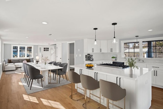 kitchen featuring pendant lighting, sink, light hardwood / wood-style flooring, white cabinetry, and a kitchen island