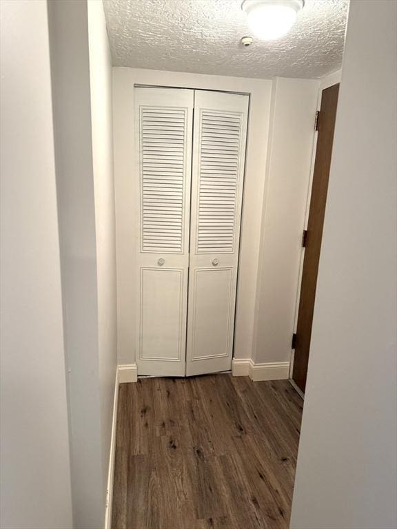 hallway featuring a textured ceiling, dark wood-style flooring, and baseboards