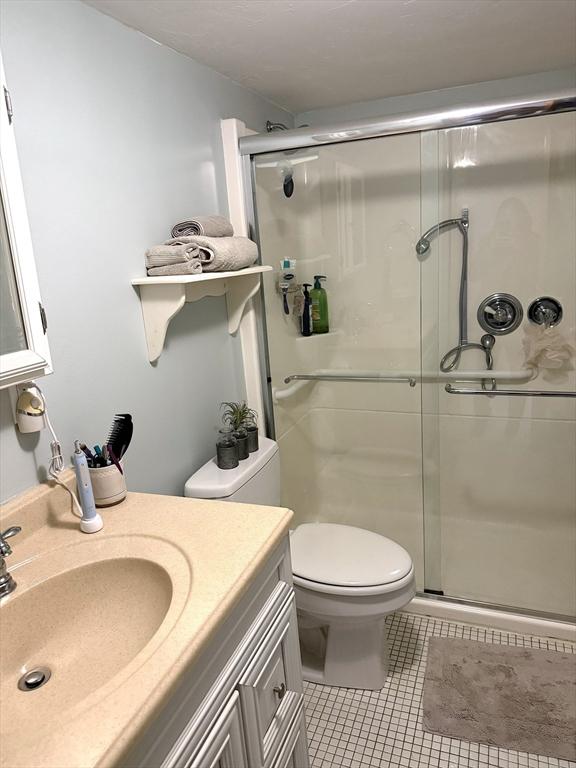 bathroom with toilet, a stall shower, tile patterned flooring, and vanity