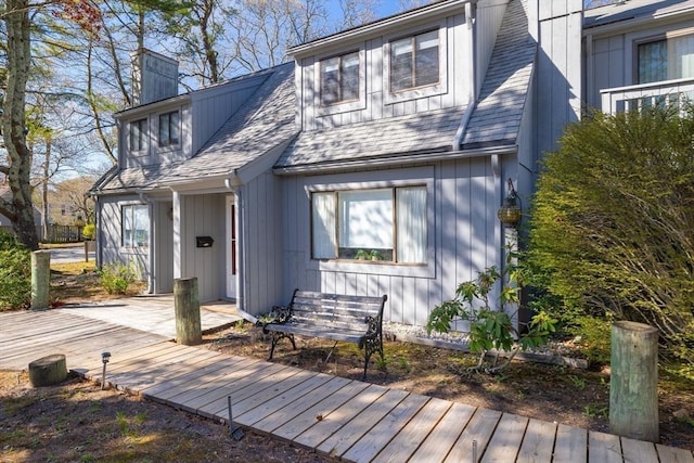 view of front of house with roof with shingles, a wooden deck, and a chimney