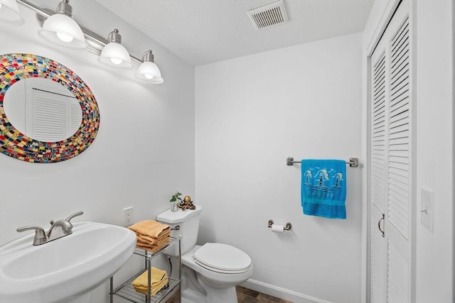 bathroom featuring visible vents, a closet, toilet, baseboards, and a sink