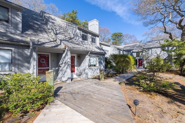 exterior space with board and batten siding, a chimney, roof with shingles, and a wooden deck