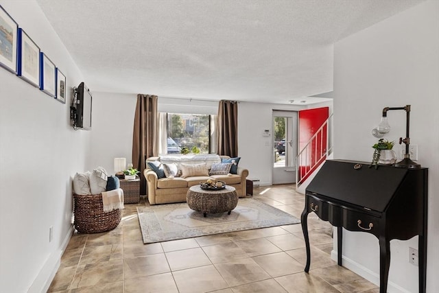living area featuring baseboards, a textured ceiling, light tile patterned floors, and stairway