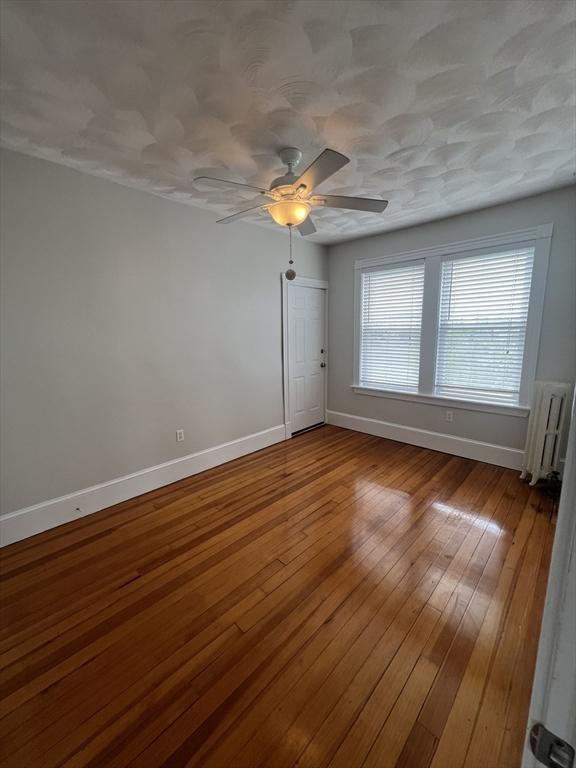 unfurnished room featuring baseboards, radiator, wood-type flooring, and a ceiling fan