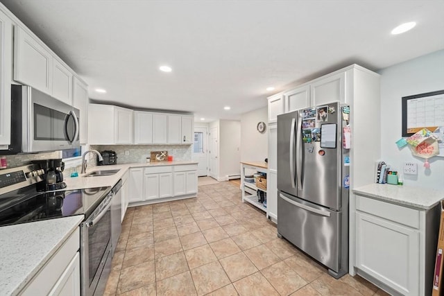 kitchen with sink, appliances with stainless steel finishes, white cabinetry, backsplash, and light stone countertops