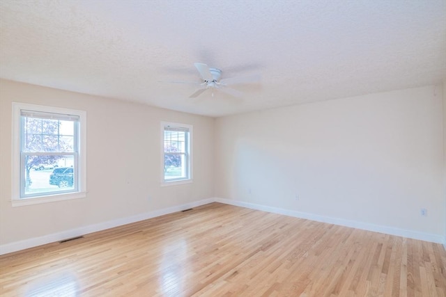 empty room with light wood-type flooring, healthy amount of natural light, baseboards, ceiling fan, and a textured ceiling