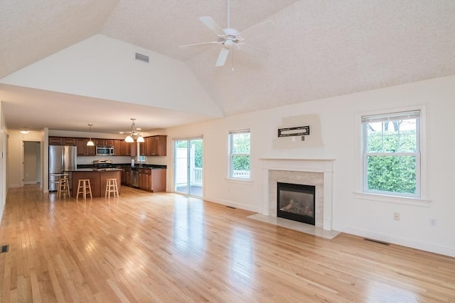 unfurnished living room featuring light wood-style flooring, a fireplace with flush hearth, a ceiling fan, baseboards, and high vaulted ceiling