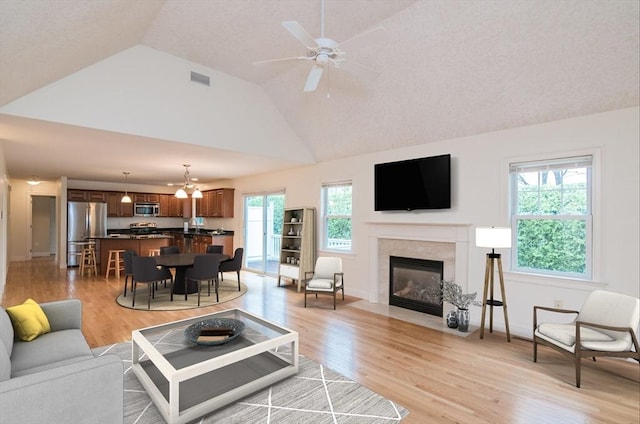 living area featuring lofted ceiling, light wood-type flooring, a high end fireplace, ceiling fan, and baseboards