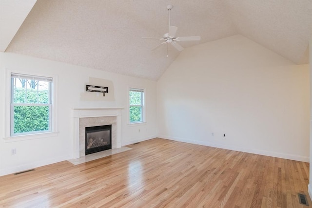 unfurnished living room featuring vaulted ceiling, light wood-style flooring, ceiling fan, a tile fireplace, and baseboards