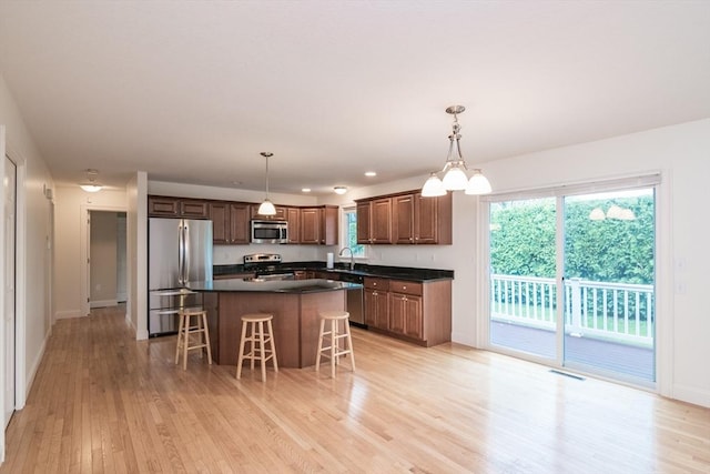 kitchen featuring stainless steel appliances, a sink, dark countertops, light wood-style flooring, and recessed lighting