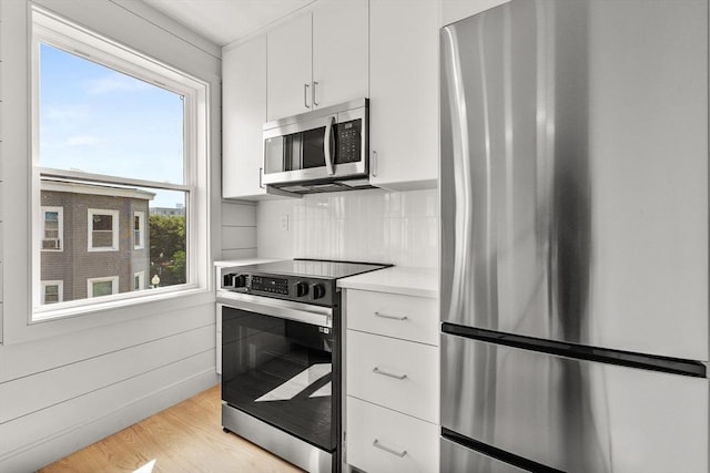 88 Maverick St Unit 3, Boston, MA 02128 - kitchen with stainless steel appliances, light countertops, white cabinets, light wood finished floors, and decorative backsplash