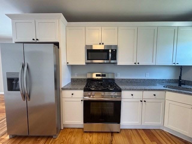 404 Brayton Ave, Fall River, MA 02721 - kitchen with appliances with stainless steel finishes, light wood finished floors, white cabinets, and dark stone counters