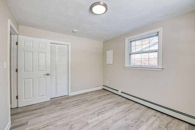 unfurnished bedroom featuring a baseboard heating unit, a closet, light wood-style floors, and baseboards