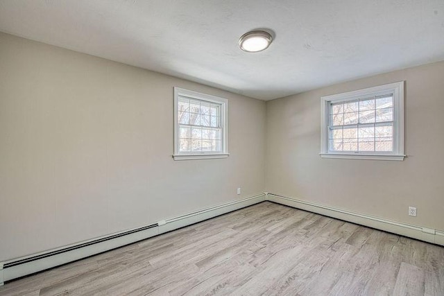 spare room with light wood-type flooring, a baseboard heating unit, and a wealth of natural light