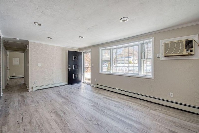 spare room featuring a baseboard heating unit, a textured wall, light wood-style flooring, and attic access