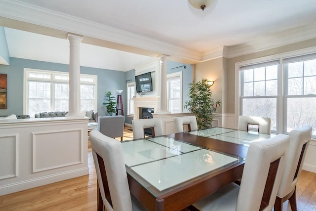 dining area featuring light wood-type flooring, ornamental molding, and ornate columns