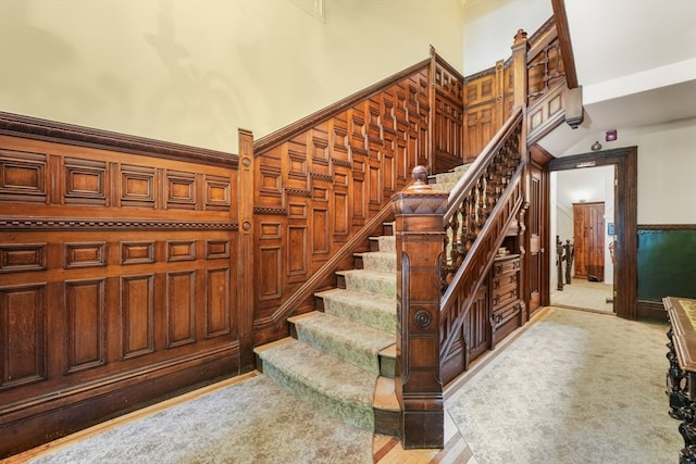 staircase with carpet floors, wooden walls, and a towering ceiling