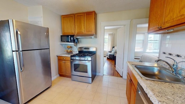 31-33 Harvard St, Medford, MA 02155 - kitchen featuring appliances with stainless steel finishes, under cabinet range hood, brown cabinetry, a baseboard heating unit, and backsplash