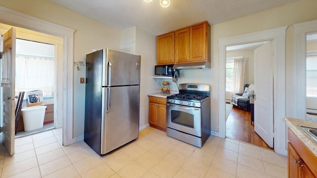 31-33 Harvard St, Medford, MA 02155 - kitchen featuring stainless steel appliances, under cabinet range hood, brown cabinetry, and light stone counters