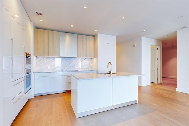 kitchen featuring light brown cabinetry, sink, white cabinetry, light hardwood / wood-style floors, and decorative backsplash