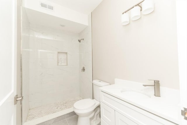 bathroom with vanity, toilet, tiled shower, and tile patterned flooring