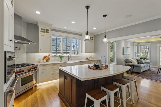 kitchen with premium range, glass insert cabinets, wall chimney exhaust hood, and a sink