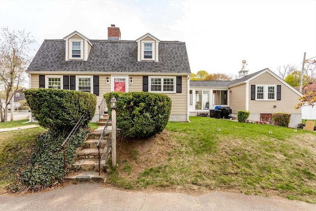 cape cod-style house featuring a chimney, a front yard, and roof with shingles