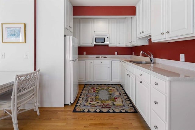 kitchen with white cabinets, white appliances, light hardwood / wood-style floors, and sink