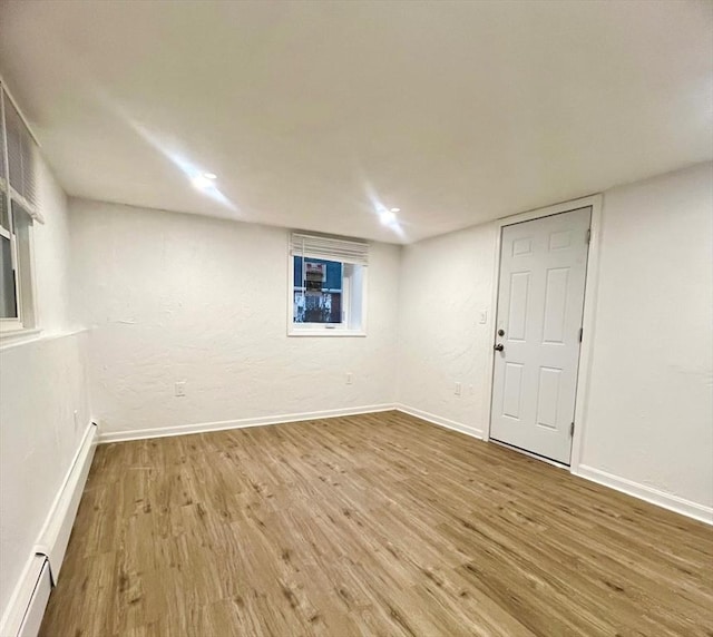 spare room featuring a baseboard heating unit, wood finished floors, and baseboards