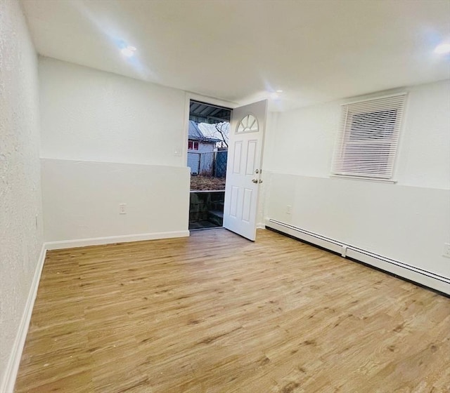 empty room featuring a baseboard heating unit, baseboards, and light wood finished floors