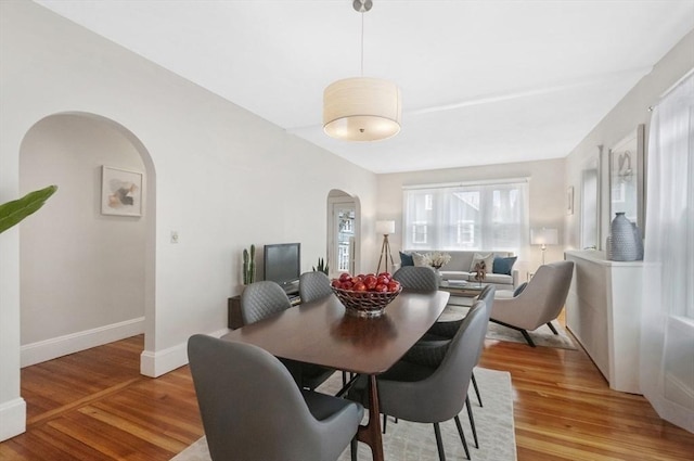 dining room featuring arched walkways, light wood finished floors, and baseboards