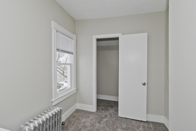 unfurnished bedroom featuring carpet floors, radiator heating unit, a textured ceiling, and a spacious closet