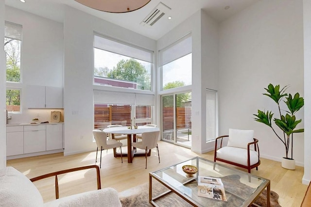 living area with a towering ceiling, plenty of natural light, light wood-style flooring, and baseboards