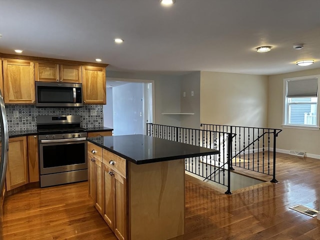 kitchen with a kitchen island, appliances with stainless steel finishes, wood-type flooring, and decorative backsplash