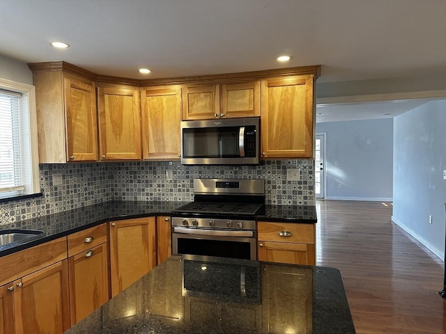 kitchen with dark stone counters, appliances with stainless steel finishes, backsplash, and dark hardwood / wood-style floors