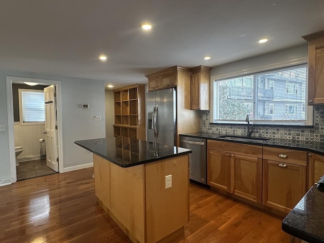 kitchen featuring stainless steel appliances, sink, a center island, dark stone counters, and dark hardwood / wood-style floors